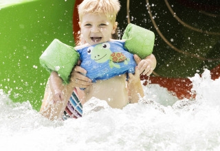 Un niño sonriente con flotadores sale de un tobogán de agua en Beach chalet del Camping 't Veld en los Países Bajos.