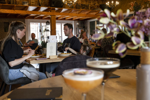 Mensen dineren en drinken in een gezellig restaurant bij een glamping accommodatie met houten interieur.
