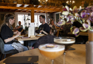 Mensen dineren en drinken in een gezellig restaurant bij een glamping accommodatie met houten interieur.