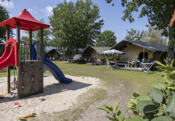 Playground with slide and Comfort safari tents at Campsite 't Veld in the Netherlands, families relaxing.