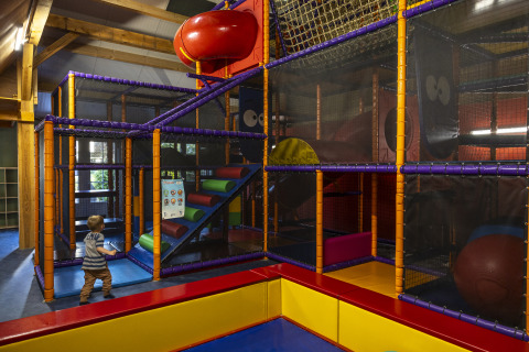 Parque infantil interior con estructuras coloridas y un niño en Comfort safari tent en Camping 't Veld.