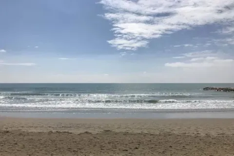Playa tranquila en Dune Agriturismo, Véneto, Italia, con arena, olas suaves y cielo parcialmente nublado.