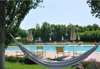 Hamac avec vue sur la piscine, transats et parasols au Dune Agriturismo, parc de vacances en Vénétie, Italie.