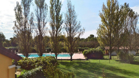 Vue de la piscine et des espaces verts avec de grands arbres au Dune Agriturismo, parc de vacances en Vénétie, Italie.