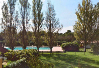 Vista de la piscina y áreas verdes con árboles altos en Dune Agriturismo, parque vacacional en Véneto, Italia.