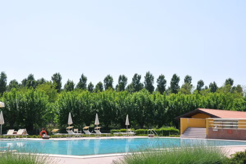 Außenpool mit Liegestühlen, Sonnenschirmen und grünen Bäumen im Dune Agriturismo in Venetien, Italien.