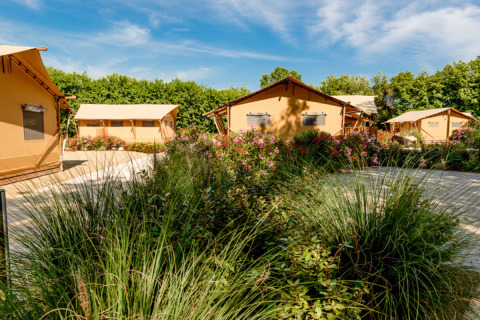 Feriepark Dune Agriturismo i Veneto, Italien, med telthytter, blomster og grønne omgivelser under blå himmel.