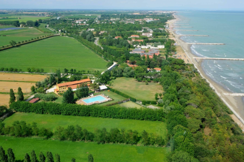 Luftfoto af Dune Agriturismo feriepark i Veneto, Italien, med pool, grønne marker og strand ved havet.