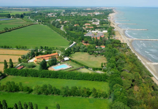 Vista aérea del parque vacacional Dune Agriturismo en Véneto, Italia, con piscina, campos y la costa.