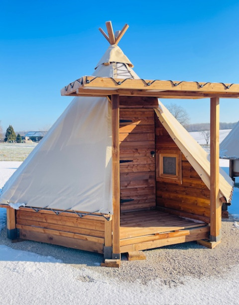 Wooden tent cabin with a canvas roof and small window at a snowy campsite in Occitanie, France, under a clear sky.