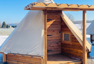 Capanna in legno con tetto in tela e finestra in un campeggio innevato in Occitania, Francia, sotto cielo sereno.
