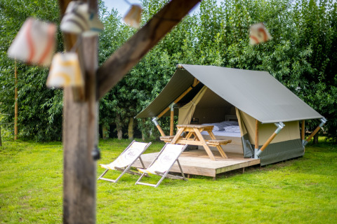 Safaritent met houten terras, ligstoelen en picknicktafel, omringd door gras en groene bomen.