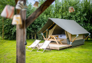 Safaritent met houten terras, ligstoelen en picknicktafel, omringd door gras en groene bomen.