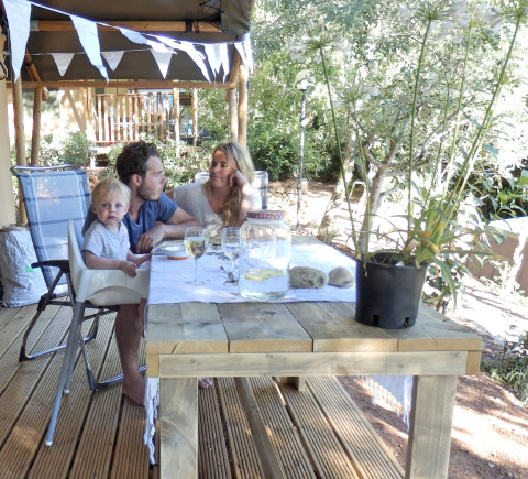 Family enjoying a meal outdoors under a safari tent at Campsite Rosselba le Palme, Italy, sunny day.
