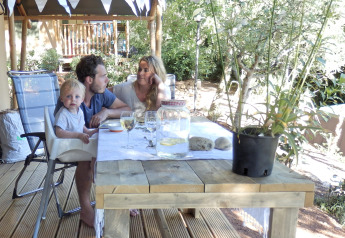 Family enjoying a meal outdoors under a safari tent at Campsite Rosselba le Palme, Italy, sunny day.