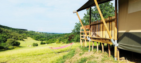 Uitzicht vanaf een safaritent met badkamer, met een hangmat en glooiende groene heuvels.