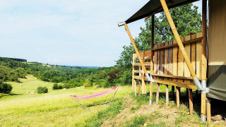 Vista da una tenda safari con bagno, con un'amaca e verdi colline in lontananza.
