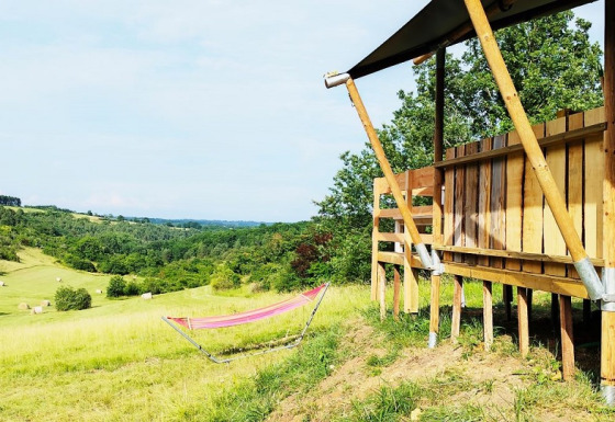 Uitzicht vanaf een safaritent met badkamer, met een hangmat en glooiende groene heuvels.