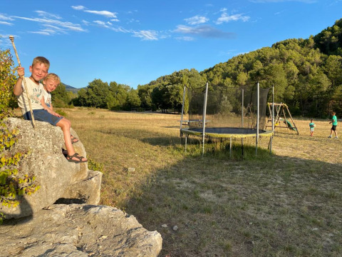 Zwei Kinder sitzen auf einem Felsen neben einem Trampolin auf dem Campingplatz Le Moulin de Cost in Frankreich.