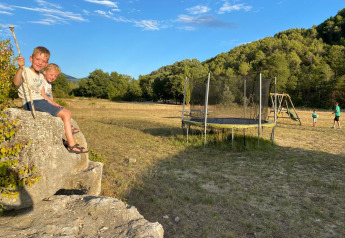 Dos niños sentados en una roca junto a una cama elástica en el camping Le Moulin de Cost en Francia.