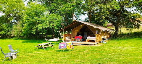 Een gezellige safaritent met veranda, hangmat, picknicktafel en stoelen op een grasveld met bomen rondom.