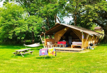 Een gezellige safaritent met veranda, hangmat, picknicktafel en stoelen op een grasveld met bomen rondom.