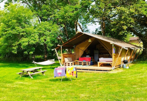Een gezellige safaritent met veranda, hangmat, picknicktafel en stoelen op een grasveld met bomen rondom.