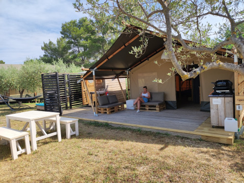 Safaritent met badkamer, houten terras, zithoek, picknicktafel en omringd door bomen.