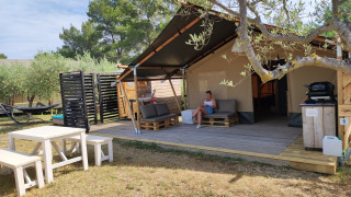 Safaritent met badkamer, houten terras, zithoek, picknicktafel en omringd door bomen.