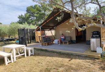 Tienda safari con baño privado, terraza amueblada, mesa de picnic y árboles alrededor del lugar.