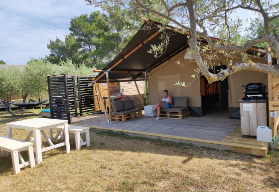 Safaritent met badkamer, houten terras, zithoek, picknicktafel en omringd door bomen.