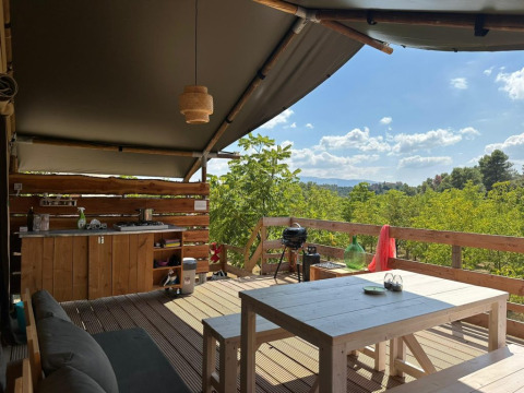 Vista desde una tienda safari Safaritent met badkamer Premium, con cocina externa y mesa, rodeada de bosque.
