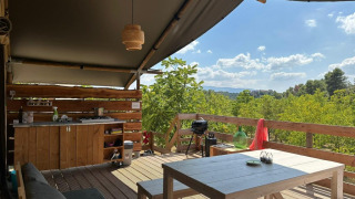 Vista dalla Safaritent met badkamer Premium con cucina all’aperto, tavolo e panorama sulla foresta.