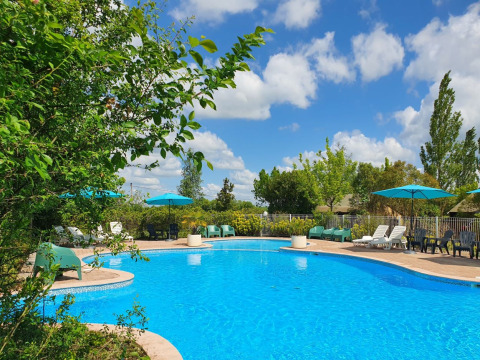 Piscina all'aperto con ombrelloni blu, lettini e alberi a Camp Redon in Occitania, Francia.