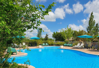 Außenpool mit blauen Sonnenschirmen, Liegestühlen und Bäumen im Camp Redon, Occitanie, Frankreich.