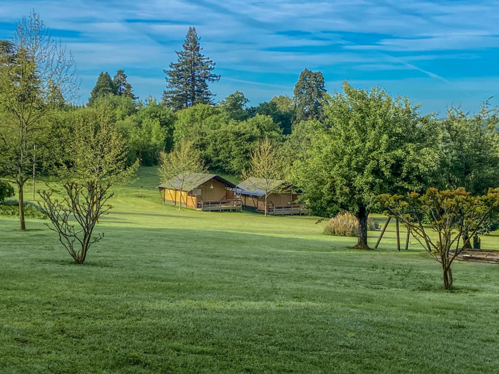 Foto van een safaritent op Camping Lestaubiere in Frankrijk, omgeven door gras en bomen.