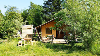 Tente safari avec salle de bain entourée d’arbres et d’herbe, mobilier extérieur devant.