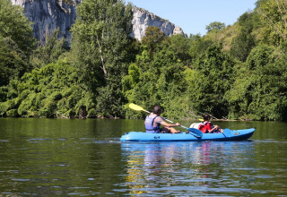 Deux personnes font du kayak sur une rivière paisible près d’un parc de vacances avec hébergement glamping.
