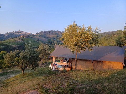 Tenda safari all’Agricampeggio Tasteria, Italia, circondata da colline verdi e un borgo distante all’orizzonte.