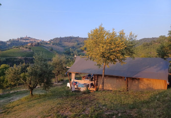 Tente safari à Agricampeggio Tasteria, Italie, entourée de collines et d’un village au loin sous un ciel bleu.