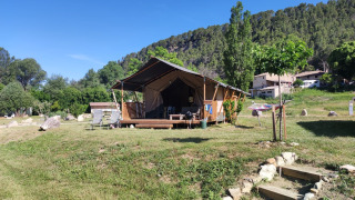 Safari-Zelt namens Lodgetent met badkamer auf einer Wiese mit Bäumen und Hügeln unter blauem Himmel.