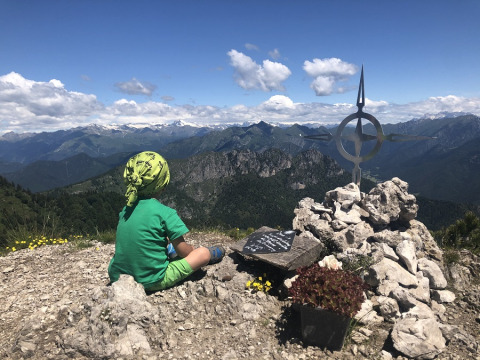Un bambino siede in cima alla montagna vicino a un ometto di pietre al Campeggio «Belvedere» in Lombardia.