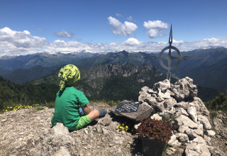 Un bambino siede in cima alla montagna vicino a un ometto di pietre al Campeggio «Belvedere» in Lombardia.