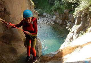 Persona con casco e giubbotto di salvataggio arrampicata su parete rocciosa al Campeggio Belvedere, Lombardia, Italia.
