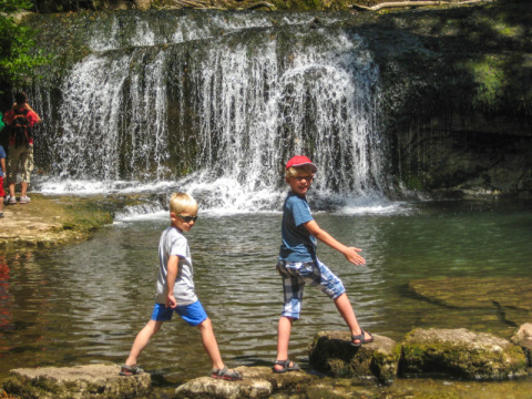 Due bambini camminano sulle rocce davanti a una cascata al campeggio «La Faz» in Bourgogne-Franche-Comté, Francia.