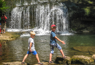 Due bambini camminano sulle rocce davanti a una cascata al campeggio «La Faz» in Bourgogne-Franche-Comté, Francia.