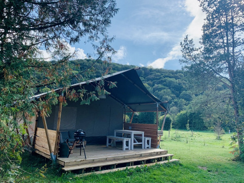 Tente safari Lodgetent XL avec salle de bain au camping La Faz en France, entourée de collines verdoyantes.