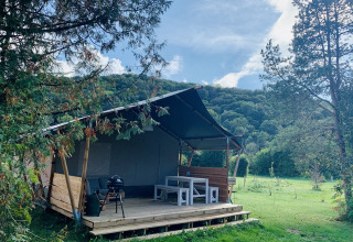 Tente safari Lodgetent XL avec salle de bain au camping La Faz en France, entourée de collines verdoyantes.