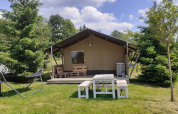 Safari tent at Campsite Les Trexons in France, with wooden furniture on grass and trees under a blue sky.
