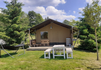 Safari tent at Campsite Les Trexons in France, with wooden furniture on grass and trees under a blue sky.